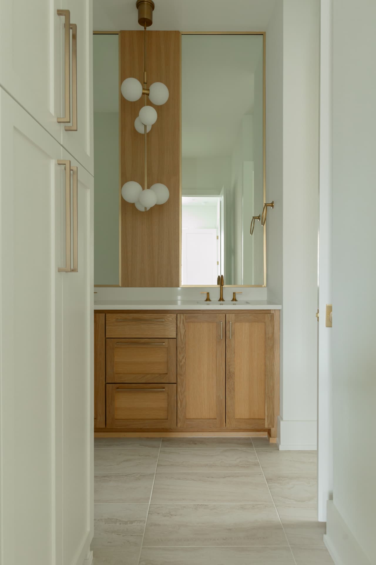 White oak vanity with brass fixtures and glass globe pendants in a Burns Construction Group custom home
