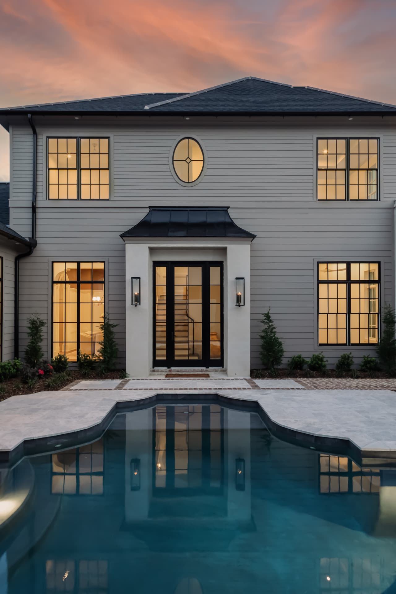 Rear elevation of a Burns Construction Group custom home at dusk with a pool and standing-seam metal roof