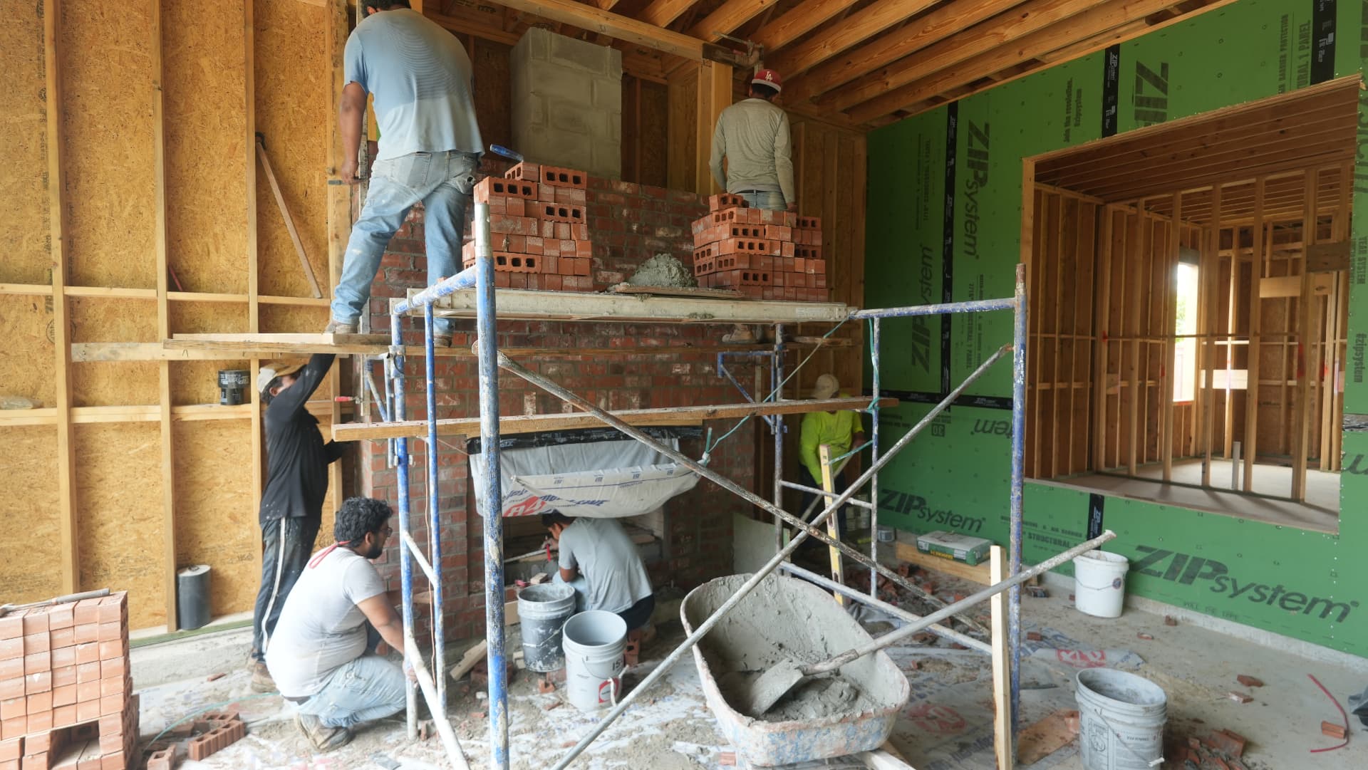 Masons building the fireplace in brick from scaffolding inside the frame.